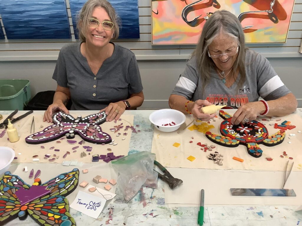 Two women create mosaic art, focusing on a butterfly and turtle design